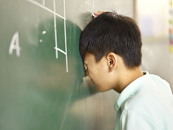 Frustrated middle schooler with head against chalkboard at school